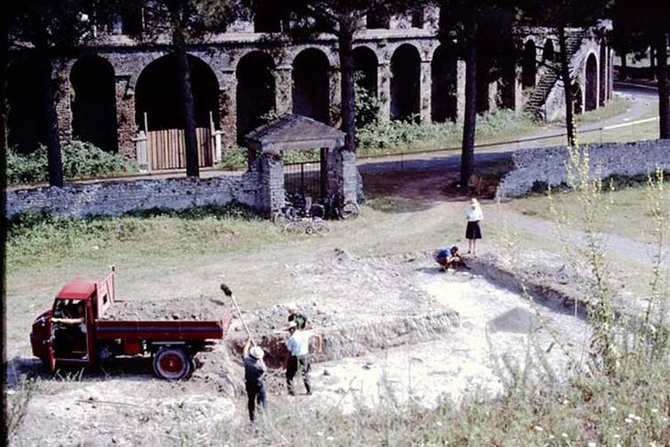 A red ute and five people working in a shallow ditch outside an amphitheatre